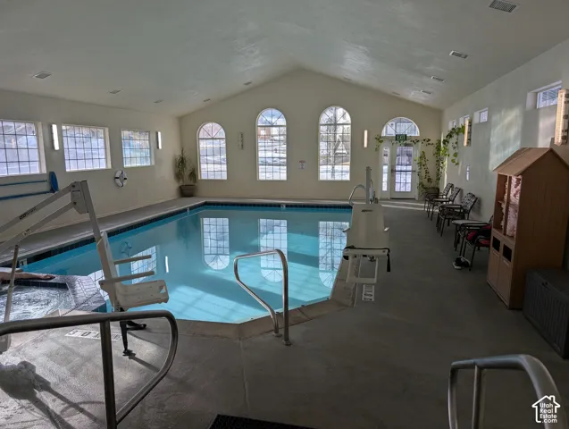 Indoor swimming pool area featuring vaulted ceilings, arched windows, recessed lighting, and an integrated spa
