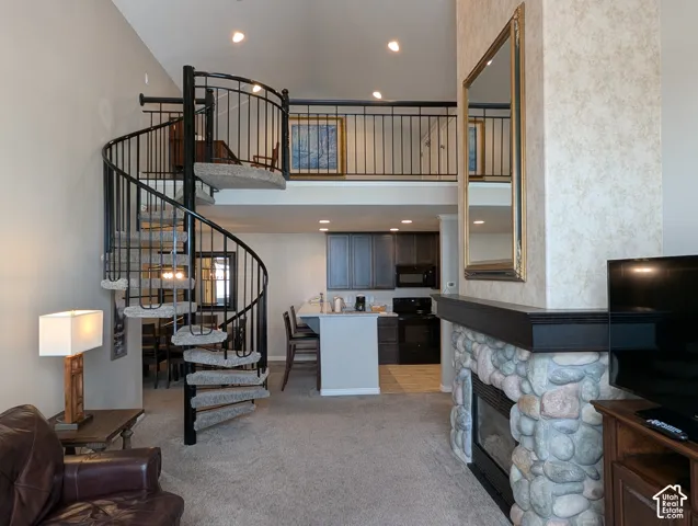 Spiral staircase with metal railing, stone fireplace featuring a dark mantle, and vaulted ceiling