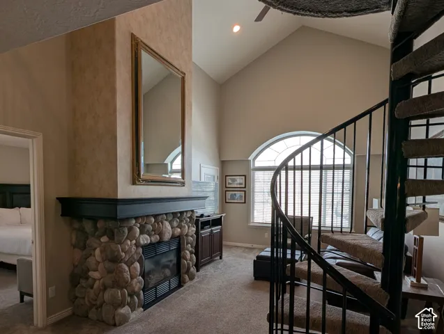 Vaulted ceiling, rock fireplace with a dark mantle, metal spiral staircase, and large arched window