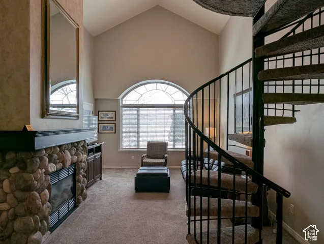 Vaulted ceiling, stone-surround fireplace, large arched window, and metal spiral staircase