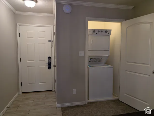 Entry door and laundry closet featuring a built-in stackable washer and dryer unit,  and neutral tile flooring