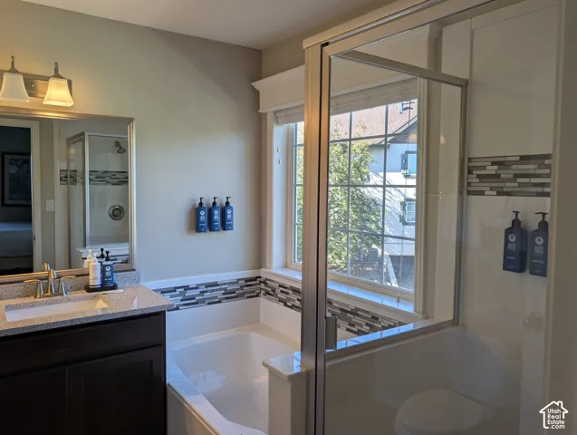 Primary bathroom featuring a soaking tub, separate glass-enclosed shower, dark wood vanity, countertop, and decorative tile