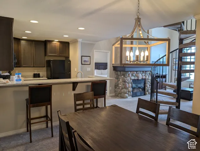 Kitchen area featuring dark cabinetry, bar, and a metal-frame pendant chandelier, complemented by a river rock fireplace and a spiral staircase.