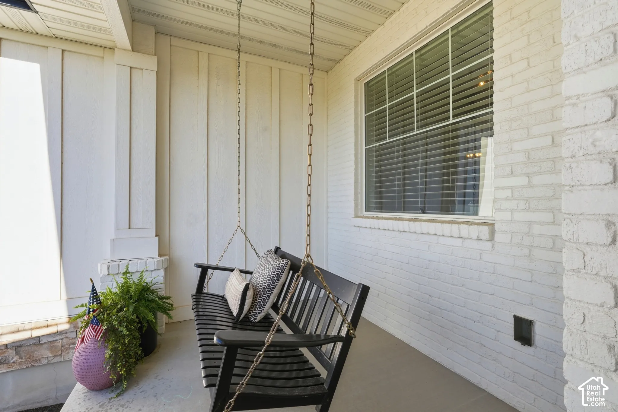 Covered front porch featuring white painted brick masonry, vertical board siding, and a concrete floor