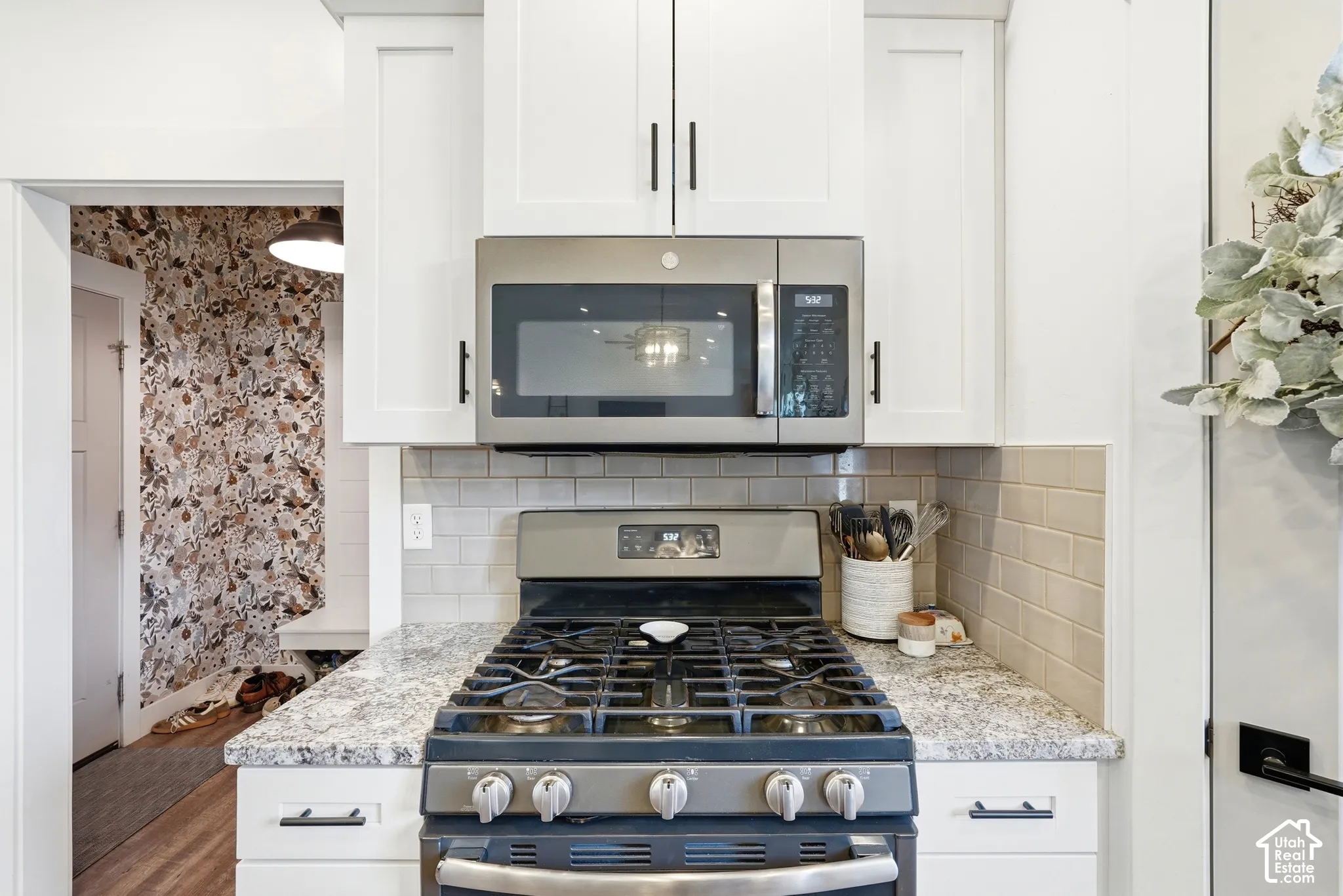 White shaker-style cabinetry, stainless steel gas range, over-the-range microwave, stone-finish countertops, and subway tile backsplash
