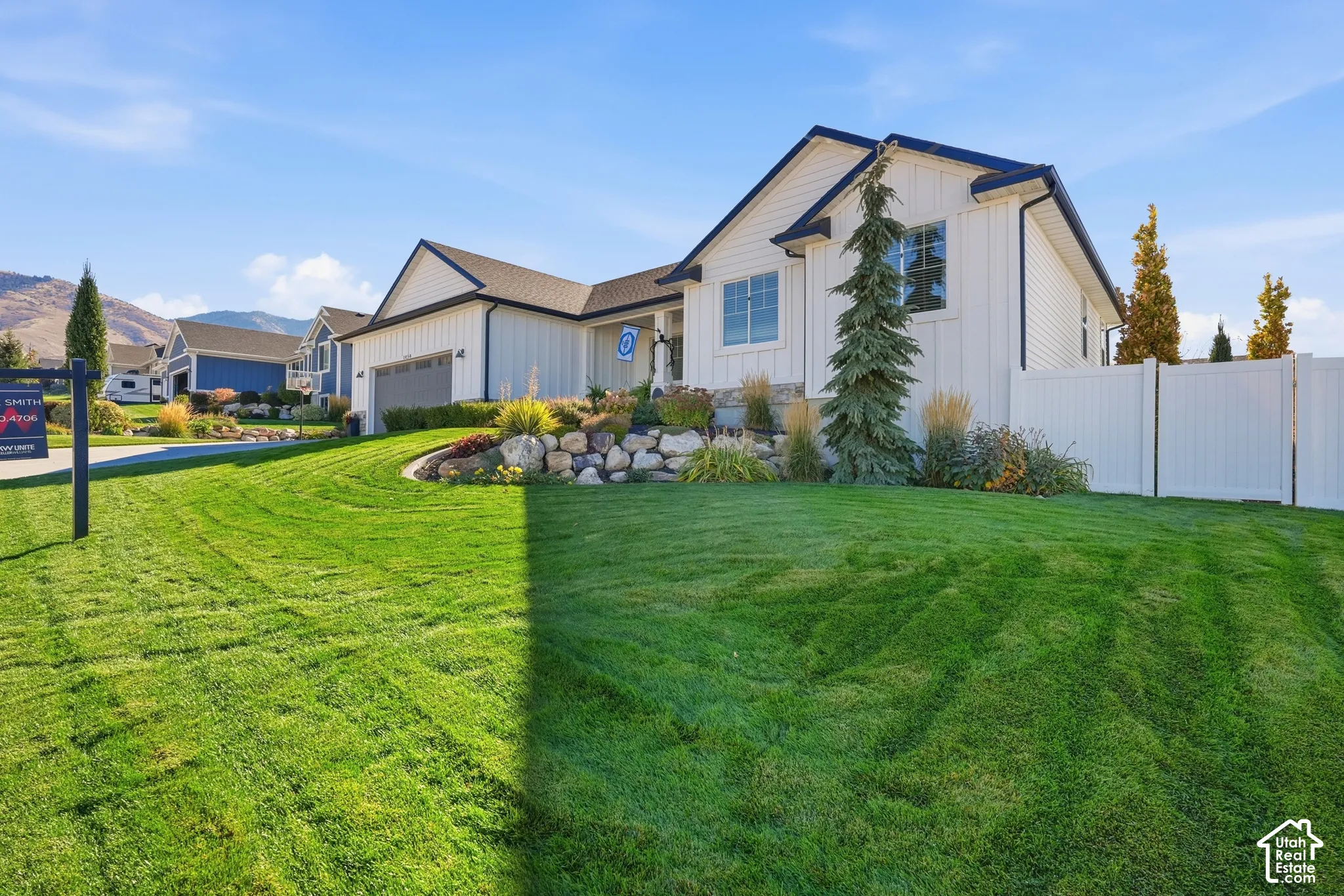 Exterior featuring vertical board-and-batten siding, a stone veneer foundation accent, a rock-retaining landscape bed, and a full-height white vinyl perimeter fence