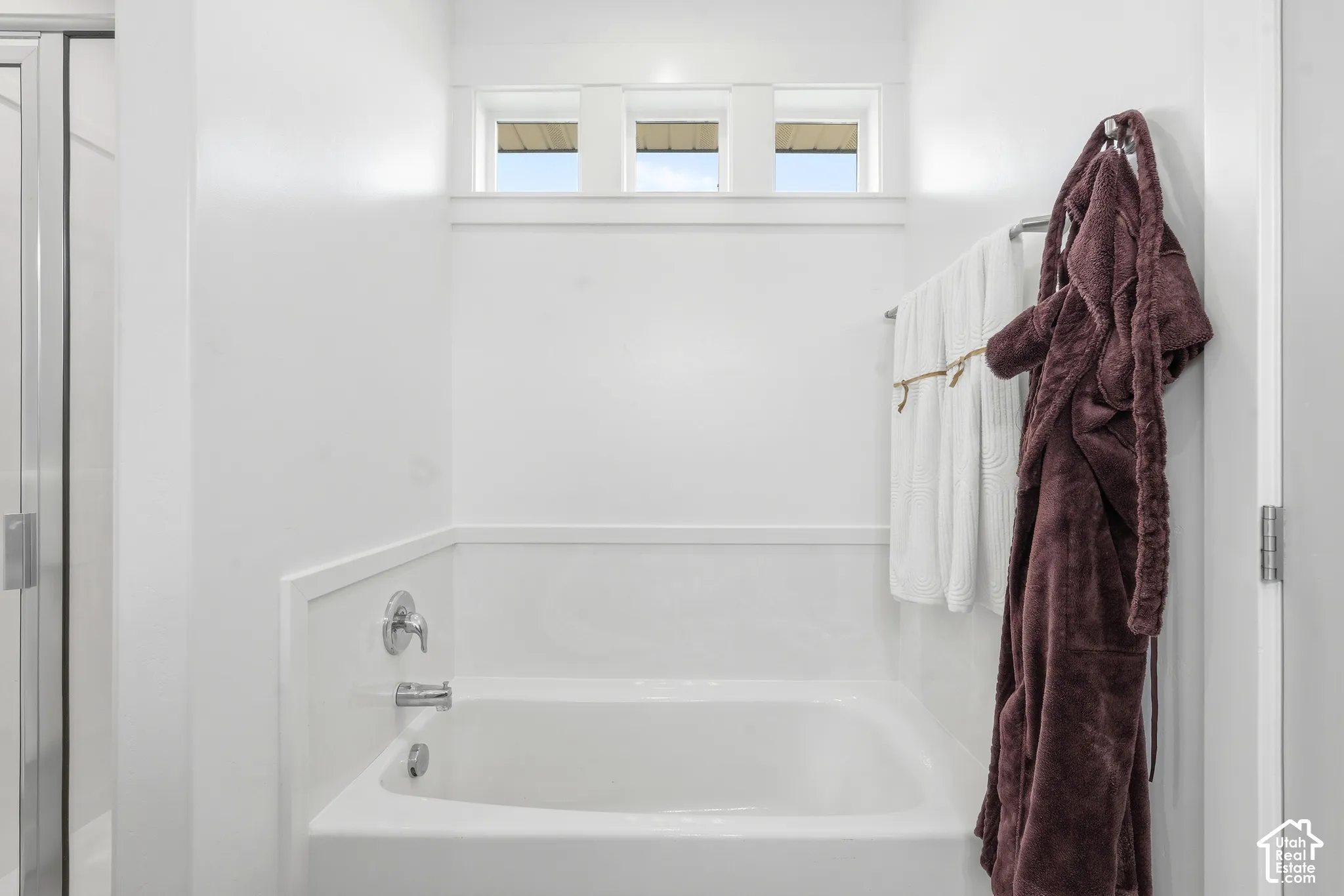 Soaking tub with chrome fixtures, three-pane transom window, and white wainscoting