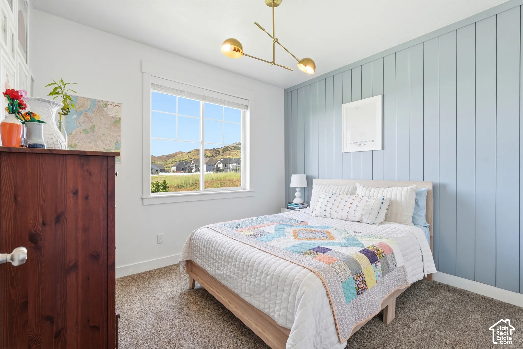 Accent wall with vertical board-and-batten detailing, gold-tone multi-arm pendant lighting, wall-to-wall carpeting, and window with exterior hillside scenery