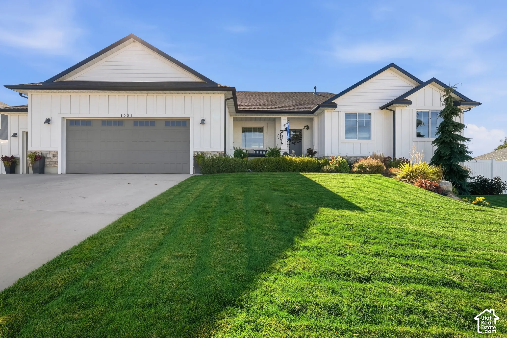 Modern farmhouse exterior featuring vertical board-and-batten siding, stone veneer accents, an attached multi-car garage, and manicured landscaping