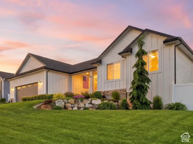 White board-and-batten siding, stone masonry accents, multi-gabled roofline, tiered rock garden, and manicured lawn