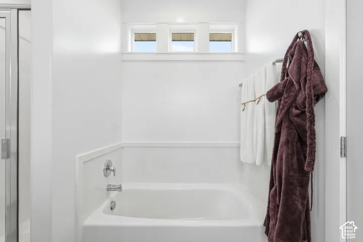 Soaking tub with chrome fixtures, three-pane transom window, and white wainscoting