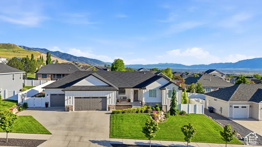 Single family. home residence with vertical siding, stone accents, three-car garage, manicured landscaping, and mountain backdrop