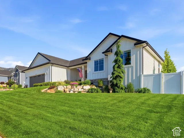 Exterior featuring white board-and-batten siding, a stone-accented landscape retaining wall, a paved driveway, and a white privacy fence against a mountain backdrop
