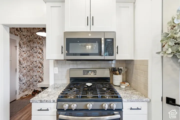 White shaker-style cabinetry, stainless steel gas range, over-the-range microwave, stone-finish countertops, and subway tile backsplash