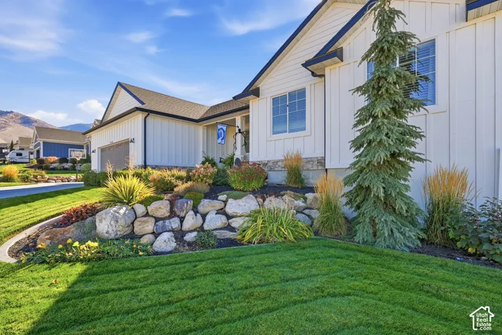 Board-and-batten exterior with stone veneer accents, multi-car garage, and landscaped rock retaining wall featuring mature shrubbery and evergreens