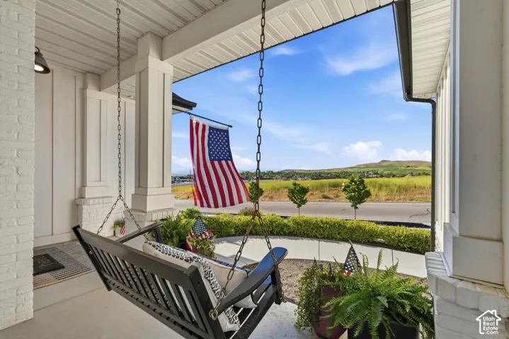 Covered front porch featuring white painted brick columns, a concrete floor, and mountainous horizon scenery