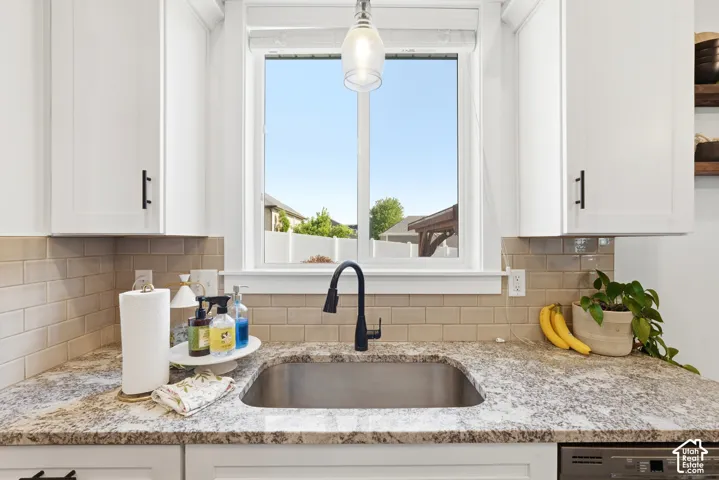 Kitchen featuring white Shaker-style cabinetry, a stone-patterned countertop, subway tile backsplash, a stainless steel undermount sink with a matte black pull-down faucet, and a pendant light fixture