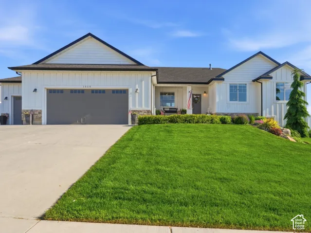 Single family residence featuring a white vertical-siding exterior, stone-veneer accents, a multi-car garage, and a manicured front lawn