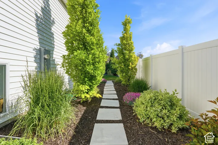 Side yard featuring horizontal siding, a white vinyl privacy fence, concrete paver path, dark organic mulch, and mature landscaping