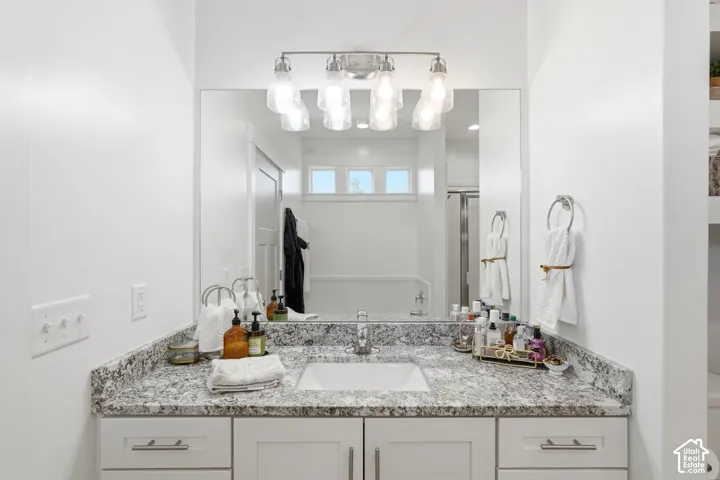 Vanity featuring a stone-pattern countertop with an integrated rectangular basin, white shaker-style cabinetry with brushed nickel hardware, a full-width wall mirror, and a four-light vanity fixture