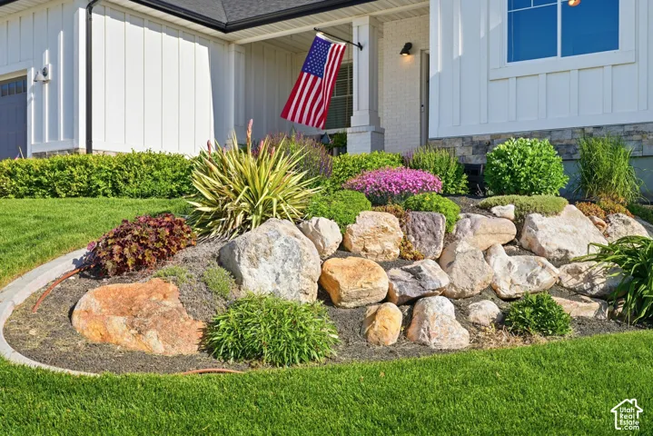 Exterior featuring white vertical siding, stone foundation accents, covered entrance, and professionally landscaped rock garden with manicured shrubs and perennial plantings