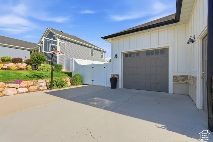 White vertical siding exterior with stone veneer accents, multi-pane third car garage door, and concrete driveway featuring a tiered landscape retaining wall