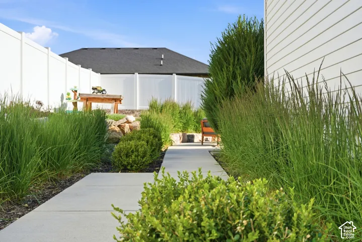 Side yard featuring a concrete pathway, full-height white vinyl privacy fencing, tiered stone retaining wall, and ornamental grasses