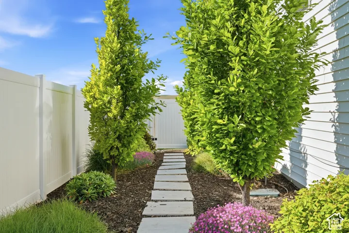 Side yard featuring a stone paver path, white vinyl privacy fencing, and mature landscaping with shrubs and ornamental trees