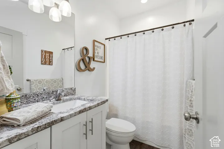 Bathroom featuring a stone-look countertop, white vanity cabinet with brushed nickel hardware, undermount sink, multi-light fixture, and tub-shower combination