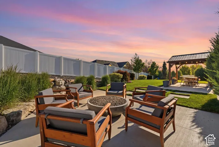 Backyard featuring a concrete patio, stone fire pit, covered wooden pergola, manicured lawn, and vinyl privacy fencing