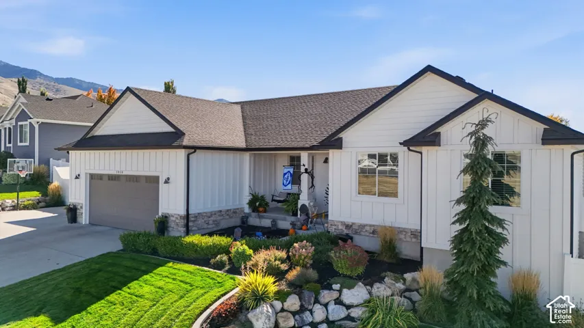 Exterior featuring vertical white siding, stone veneer accents, multi-gabled roofline, concrete driveway, and landscaped rock garden