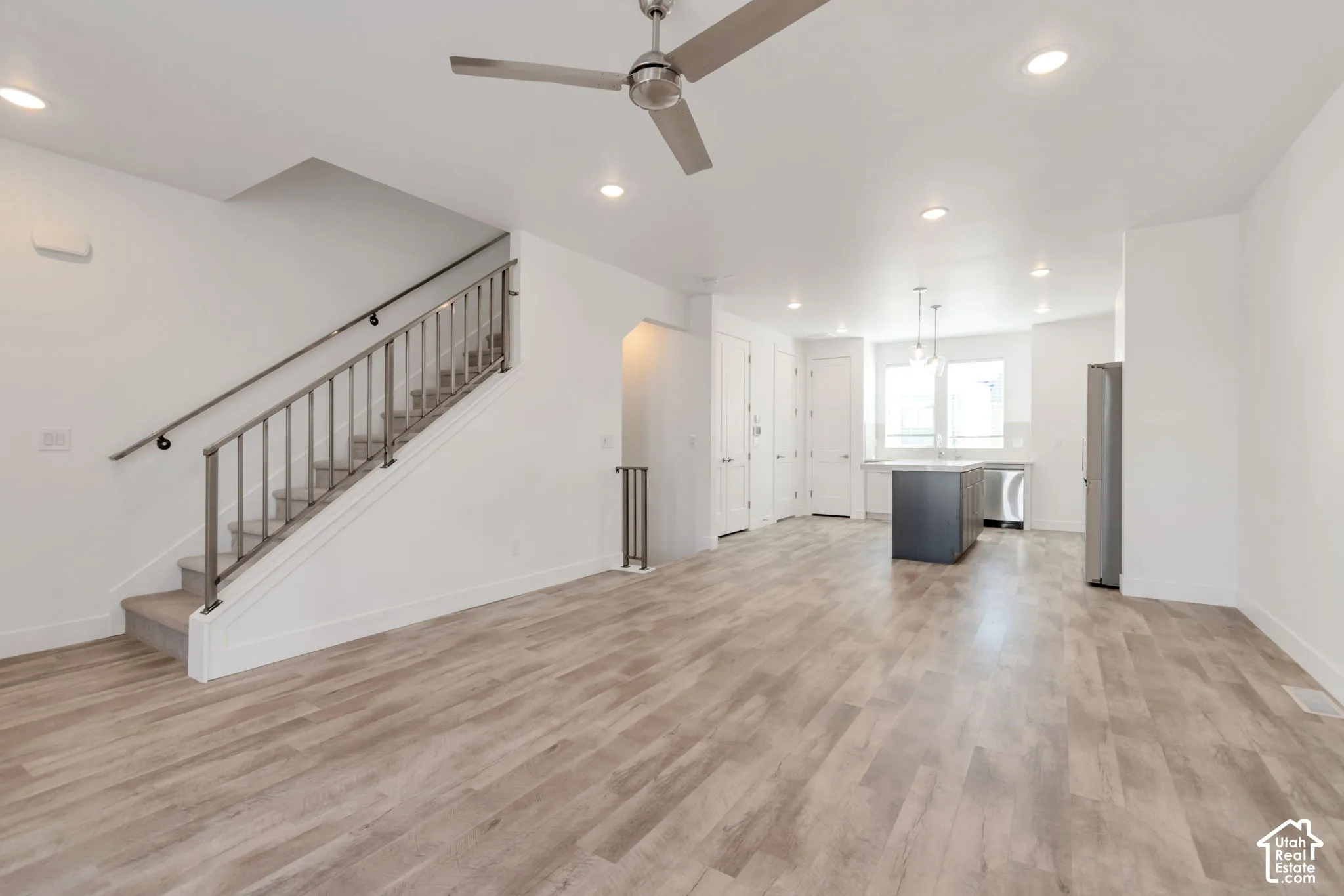 Open-concept interior featuring wood-finish flooring, recessed lighting, a modern ceiling fan, and a staircase with metal railings