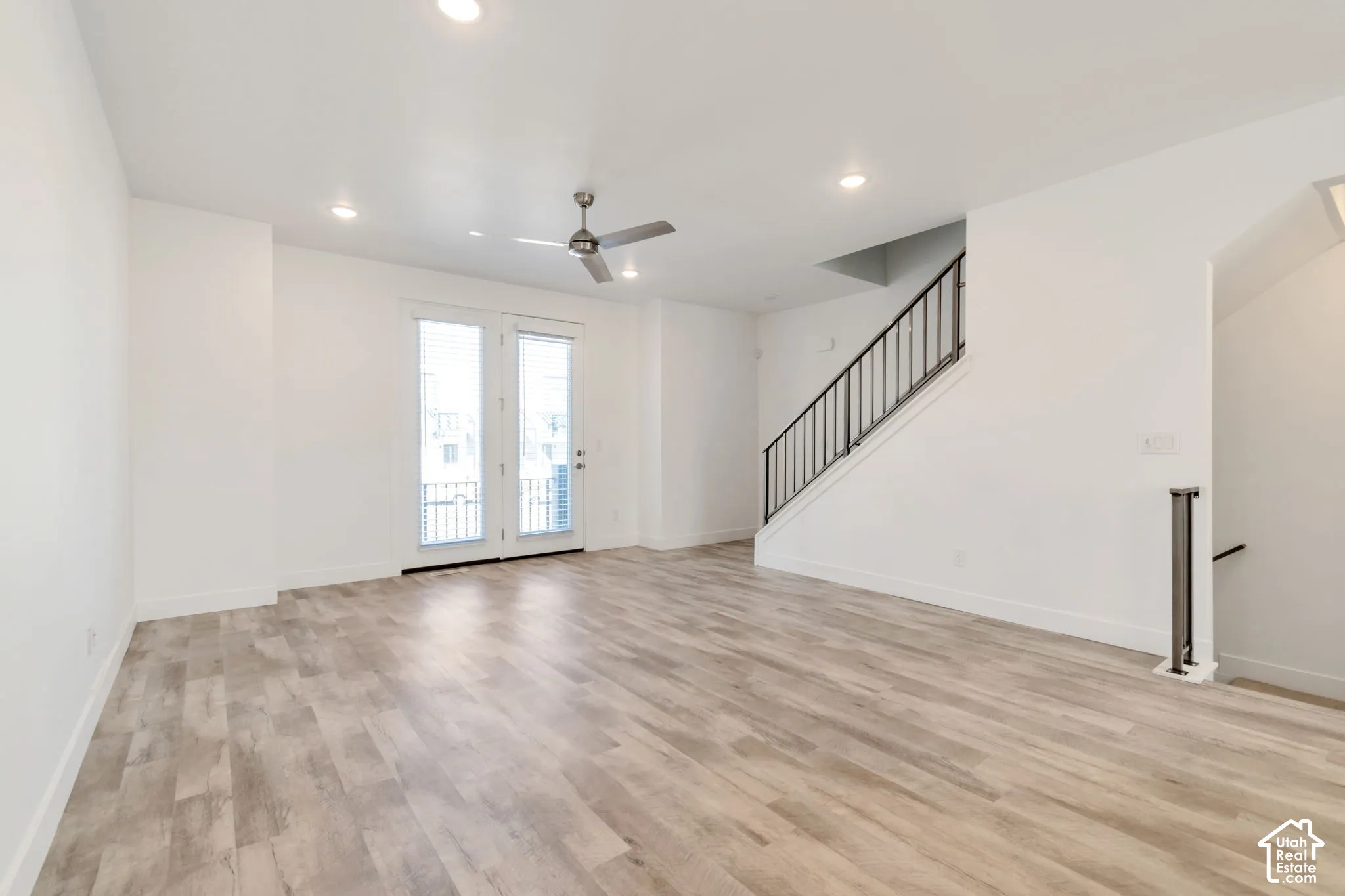 Open interior space featuring wood-finish flooring, recessed lighting, a ceiling fan, dual glass-panel entry doors, and a metal-railed staircase