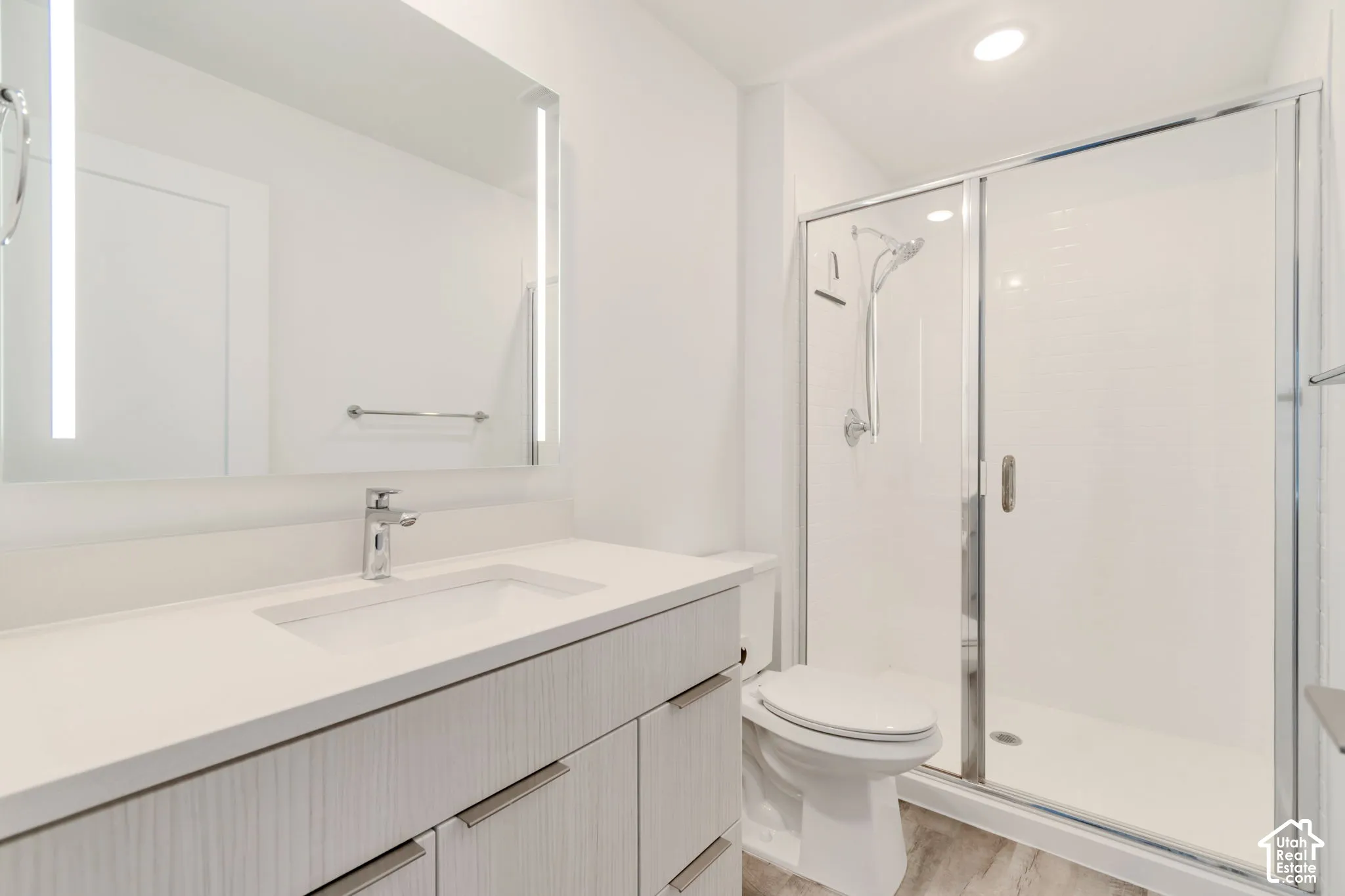 Bathroom featuring a vanity with light wood-finish cabinetry, an integrated white countertop and sink, a frameless LED-backlit mirror, and a walk-in shower with a chrome sliding glass enclosure