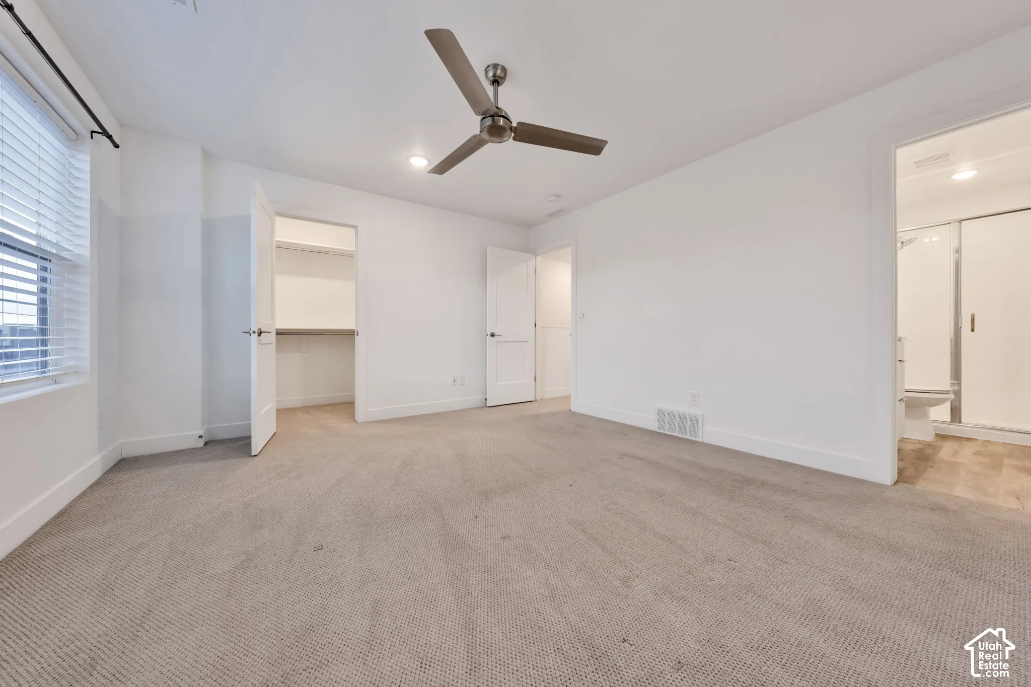 Room featuring neutral carpeting, a ceiling fan, walk-in closet with built-in shelving, and attached full bathroom