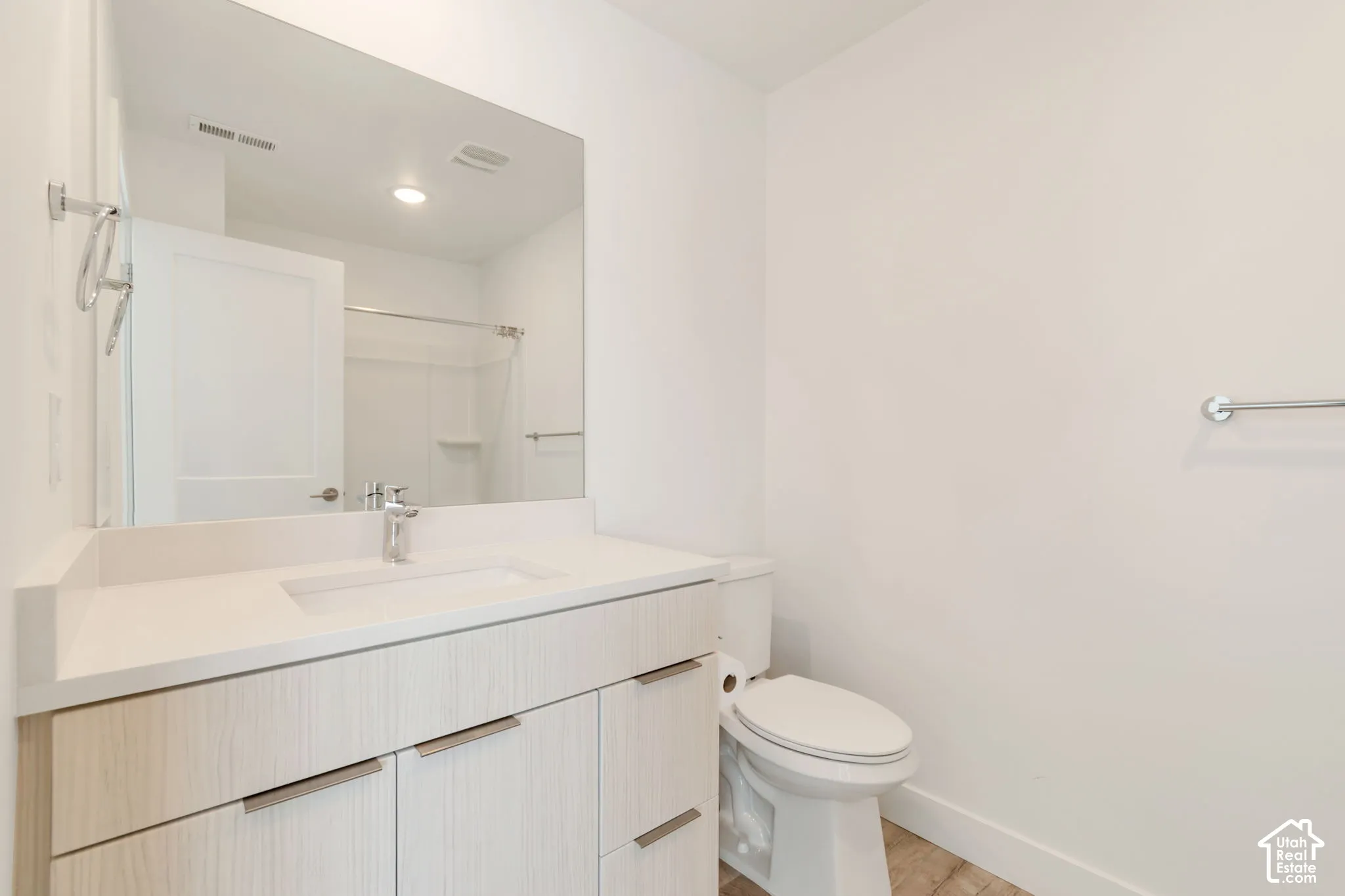 Bathroom featuring a light-toned wood-finish vanity, integrated countertop with rectangular basin, large wall-mounted mirror, and chrome finish hardware