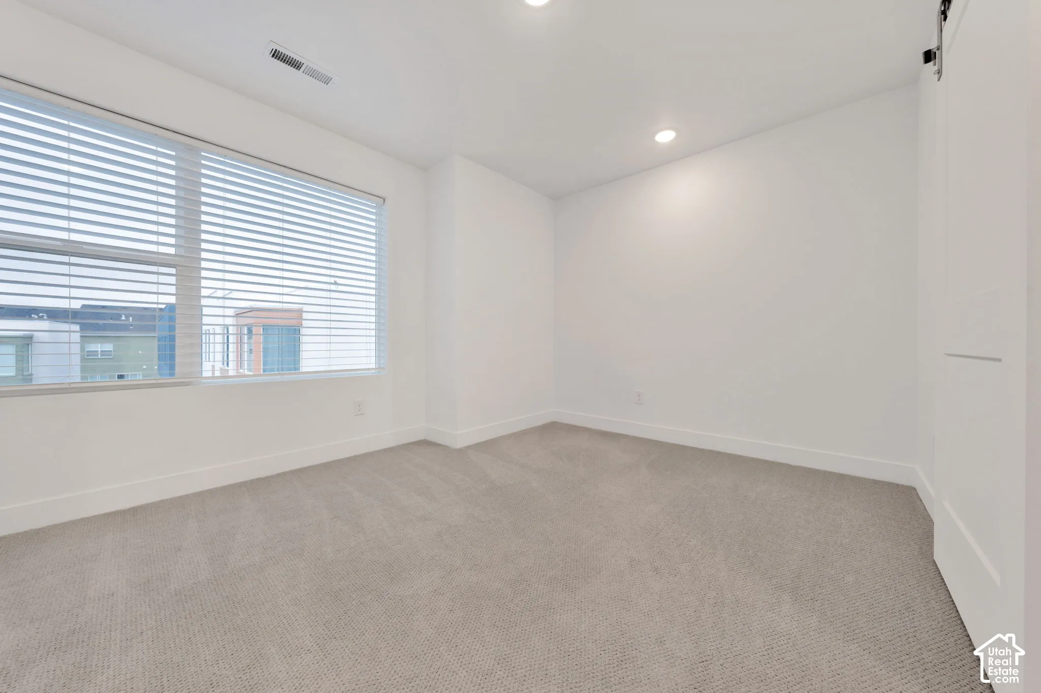 Neutral-toned carpeting, recessed ceiling lighting, and a window featuring horizontal blinds