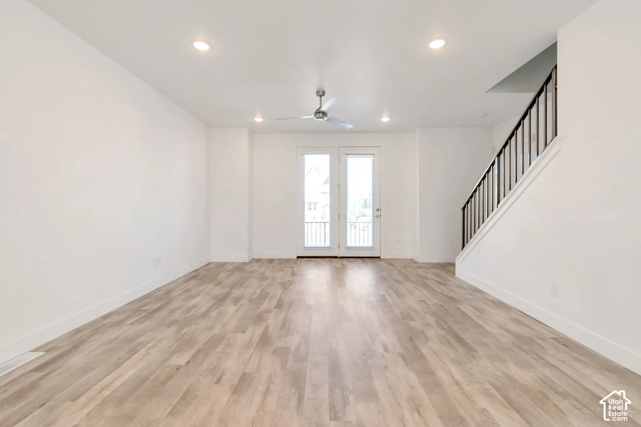 Open interior featuring wood-finish flooring, recessed lighting, a ceiling fan, dual glass-paned doors, and a staircase with a black metal railing