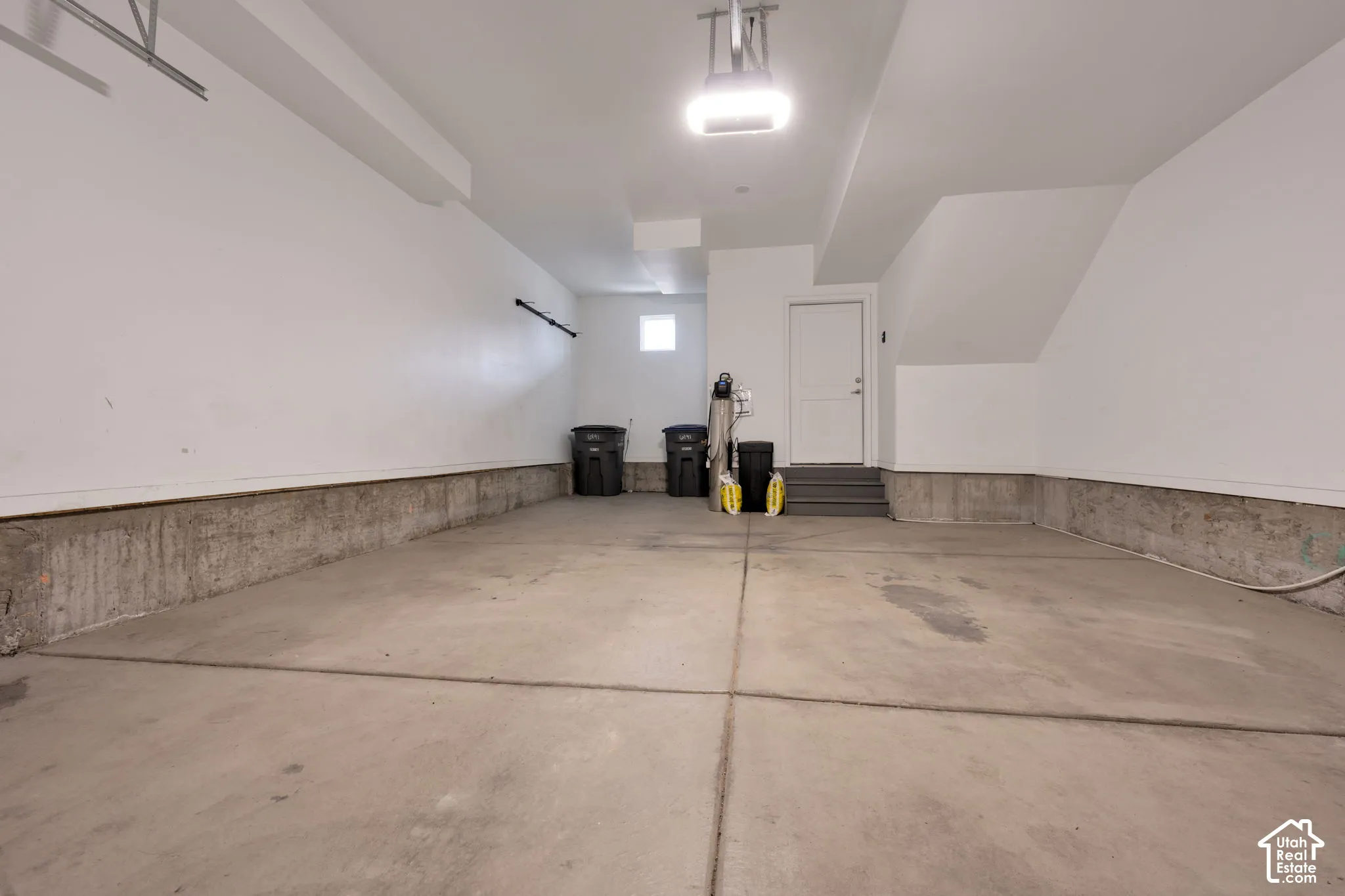 Finished garage with concrete flooring, smooth wall finishes, overhead lighting, and an access door with stairs