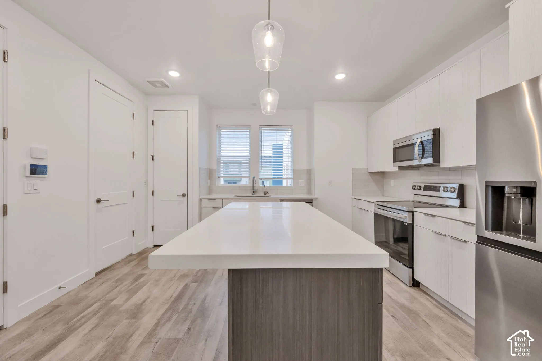 Kitchen featuring a large island with a solid surface countertop, white shaker-style cabinetry, stainless steel appliances, and wood-finish flooring
