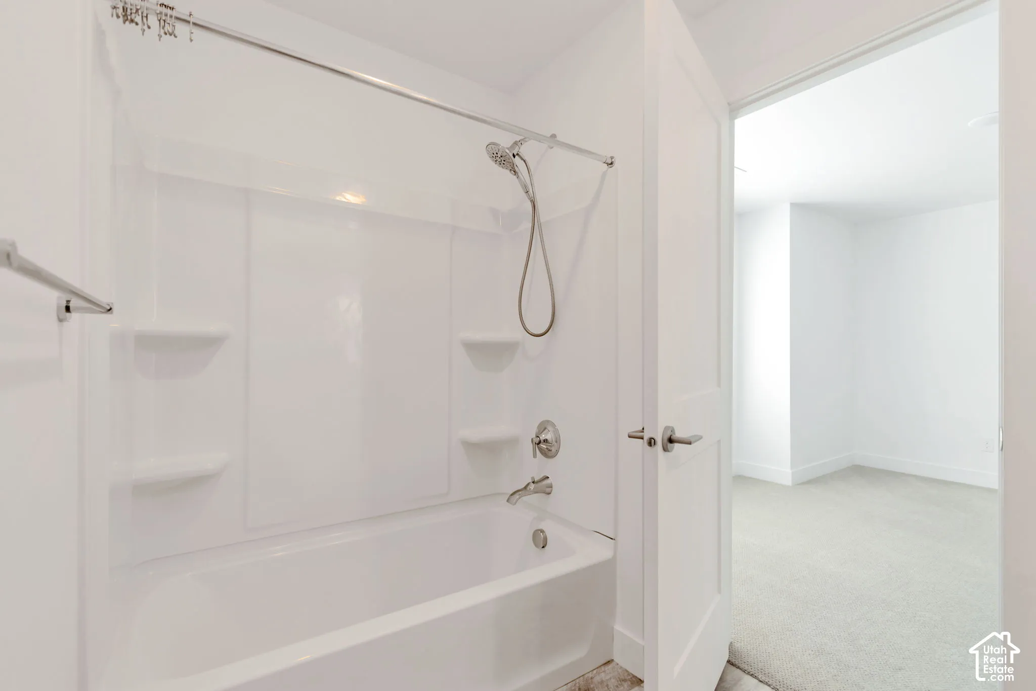 Bathroom featuring a white molded tub-and-shower surround with integrated shelving, adjustable handheld shower fixture, and polished metal hardware