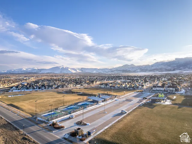 Aerial perspective of a community recreation area featuring tennis courts, a covered pavilion, open green space, and mountain backdrop
