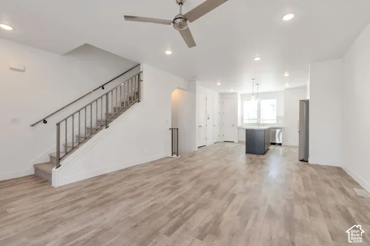 Open-concept interior featuring wood-finish flooring, recessed lighting, a modern ceiling fan, and a staircase with metal railings