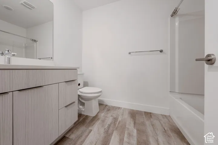 Bathroom featuring a wood-finish vanity, light-toned countertop, large wall-mounted mirror, brushed-nickel hardware, and wood-finish flooring