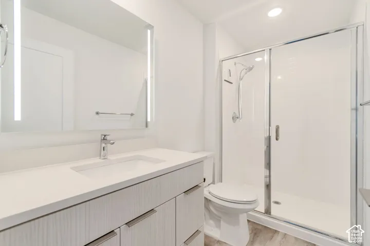 Bathroom featuring a vanity with light wood-finish cabinetry, an integrated white countertop and sink, a frameless LED-backlit mirror, and a walk-in shower with a chrome sliding glass enclosure