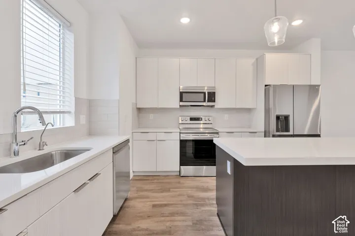 Kitchen featuring white flat-panel cabinetry, a contrasting dark island with a solid-surface countertop, stainless steel appliances, and wood-finish flooring