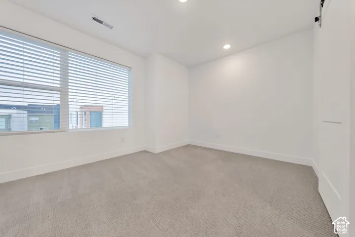 Neutral-toned carpeting, recessed ceiling lighting, and a window featuring horizontal blinds
