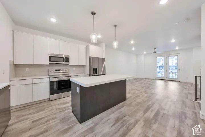 Kitchen featuring light-toned cabinetry, a center island with a solid surface countertop, stainless steel appliances, glass pendant lighting, and wood-finish flooring