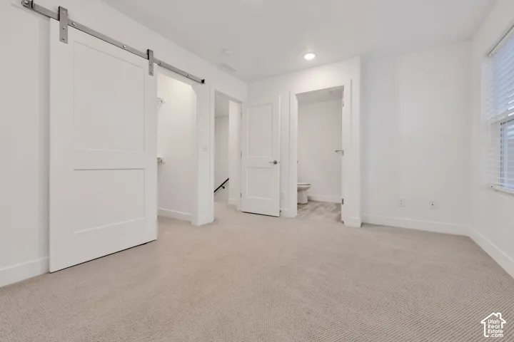 Interior space featuring a white sliding barn door on stainless steel hardware, neutral carpeting, recessed lighting, and a white two-panel door