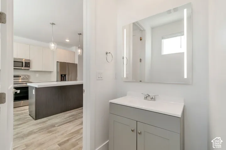 Powder room featuring a gray shaker-style vanity with a white countertop and an integrated LED-lighted mirror, paired with wood-finish flooring